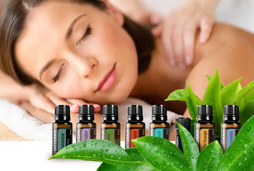 A woman is laying down and happy while receiving an AromaTouch session and in the foreground are the 8 essential oils and blends used in an AromaTouch session by doTERRA