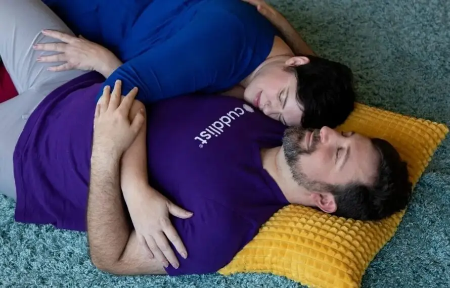 A professional cuddler wearing a purple Cuddlist shirt works with a client